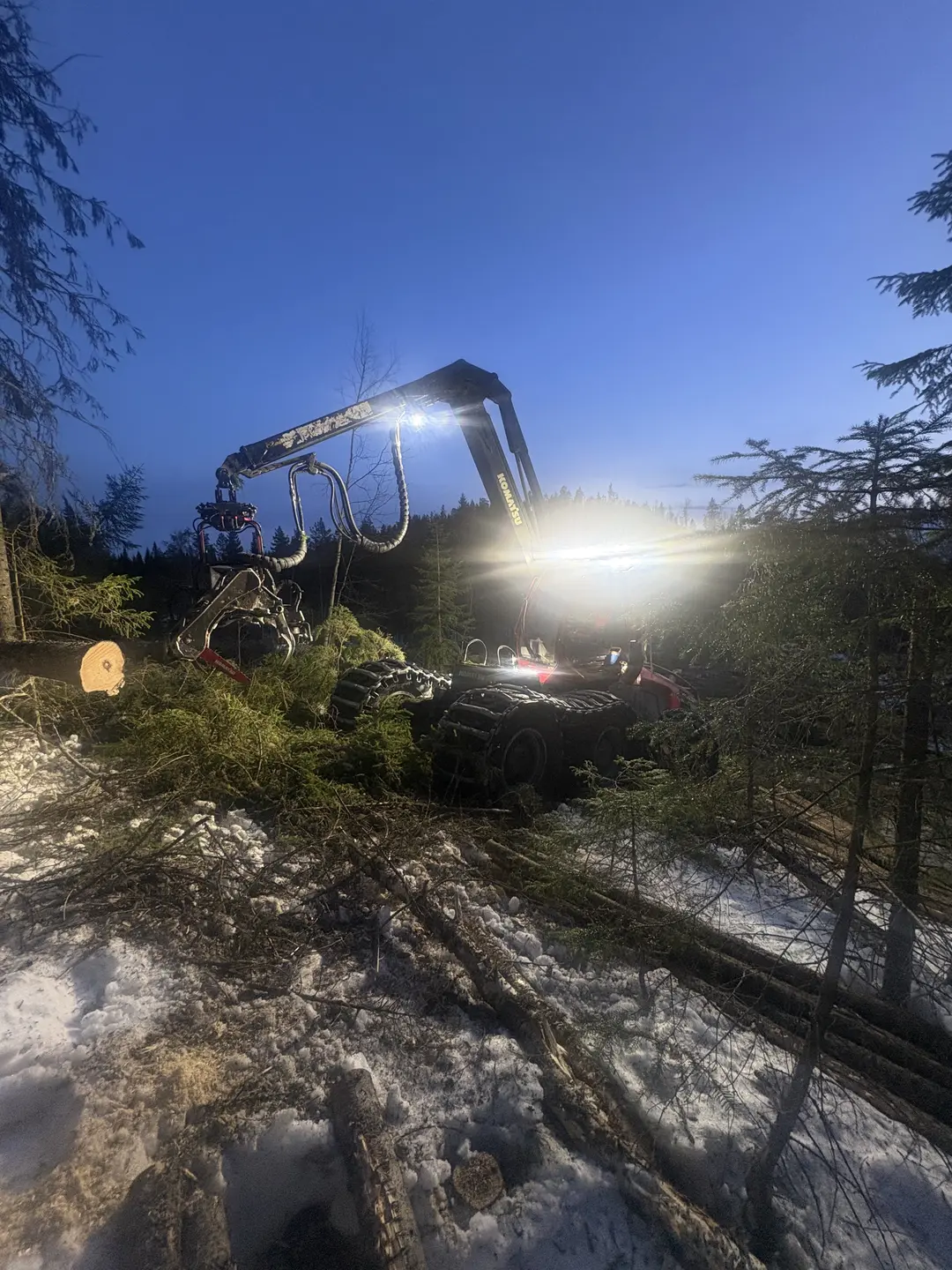 Eriks skogsmaskin arbetar i skogen under en klar vinterkväll.